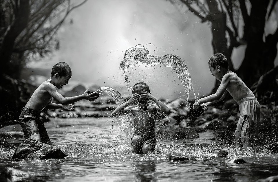 Tres niños jugando en el agua, salpicándose entre sí. Fotografía en blanco y negro.