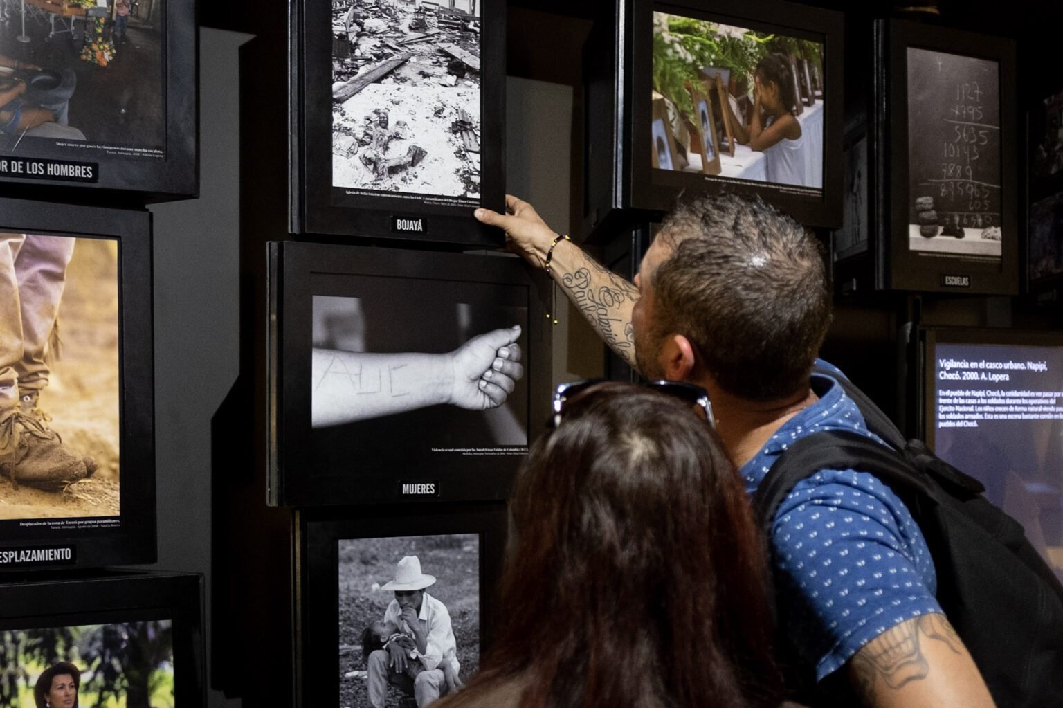 Visitantes observando fotografías en una exposición sobre el conflicto en Colombia, mostrando imágenes de Bojayá, mujeres afectadas, desplazamiento y escuelas.