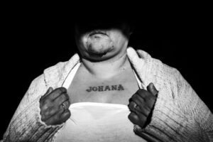 Retrato en blanco y negro de una mujer con el tatuaje 'JOHANA' en el pecho.