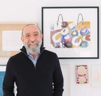 Retrato de Dani Levinas sonriendo frente a una pared con obras de arte.