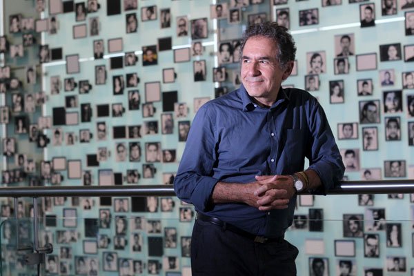 Retrato de Ricardo Brodsky de pie frente a una pared con fotografías.