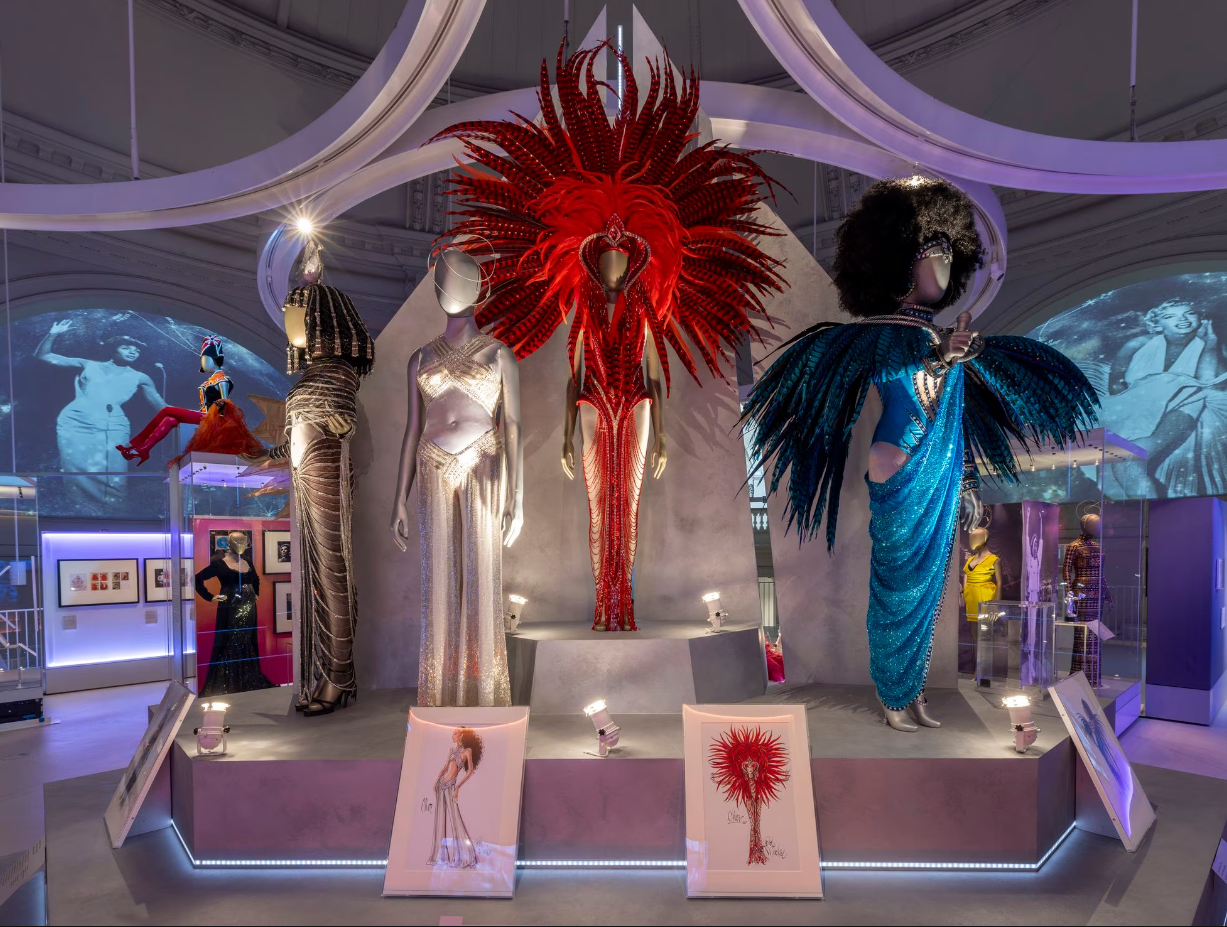 Vestuario de divas expuesto en un museo: diseños elaborados con plumas y lentejuelas en maniquíes.
