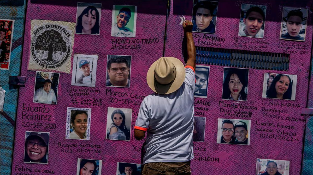 Un hombre de espaldas con sombrero coloca una de las muchas fotografías de personas desaparecidas en un muro metálico de color morado en la Glorieta de las y los Desaparecidos en México.