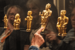 Conjunto de figuras de oro precolombinas exhibidas en un museo, con una persona señalando una de las piezas.